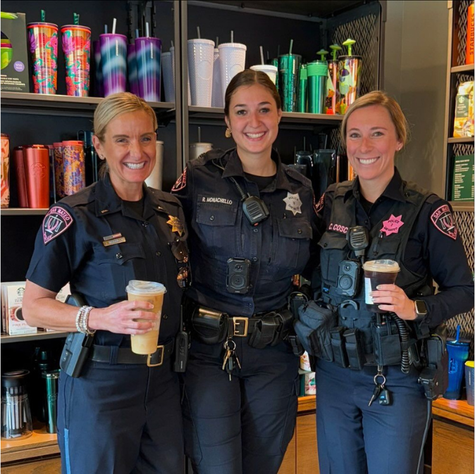 Three female police officers standing together holding coffee.